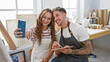 © Krakenimages.com - Smiling woman and tattooed man taking a selfie in an art studio, surrounded by paintings and supplies.