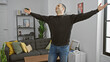 © Krakenimages.com - Joyful hispanic man celebrating inside a modern apartment living room with arms raised