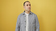 © Krakenimages.com - Hispanic man in grey shirt posing against an isolated yellow background looking away thoughtfully.