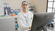 © Krakenimages.com - Hispanic scientist man in lab coat works with computer in laboratory setting, looking confident and professional.