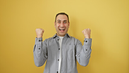 Wall Mural - Excited young hispanic man celebrating victory against a vibrant yellow background, expressing happiness and success.