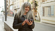 © Krakenimages.com - A mature woman with grey hair enjoys using her smartphone on a lively urban street.