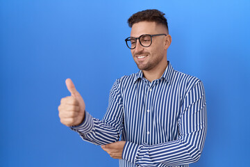 Poster - Hispanic man with beard wearing glasses looking proud, smiling doing thumbs up gesture to the side