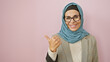 © Krakenimages.com - Smiling woman in hijab pointing sideways against a pink background, depicting positivity and guidance