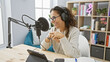 © Krakenimages.com - Hispanic woman smiling in a radio studio with microphone, headphones, tablet, and modern decor.