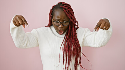 Canvas Print - Surprised black woman with braids pointing down over isolated pink background.