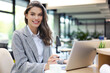 © ty - Portrait of a cheerful young businesswoman sitting at the table in office and looking at camera.