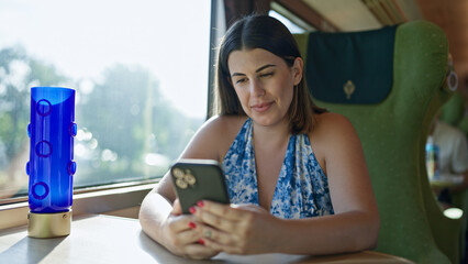 Sticker - Smiling beautiful hispanic woman sitting, happily texting on her smartphone during a modern subway ride