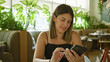 © Krakenimages.com - A young hispanic woman sitting in a cafe, smiling while using her smartphone, embodying relaxation and leisure.