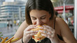 © Krakenimages.com - Young woman eating burger outdoor with city background enjoying fast food.