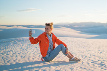 Wall Mural - hipster girl making selfie on smartphone camera sitting on white dune visiting famous white sands, f