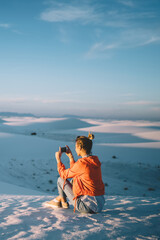 Wall Mural - young woman using smartphone for making photo of desert dunes during sunset having journey to white 