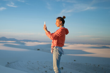 Wall Mural - hipster girl standing in white sands desert with smartphone making photos of beautiful landscape of 