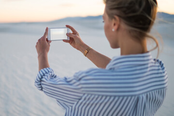 Wall Mural - back view of young woman tourist making selfie on smartphone camera exploring white sand dunes, hips
