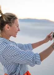 Wall Mural - smiling young blogger posing for selfie on smartphone standing in white sands national park, hipster