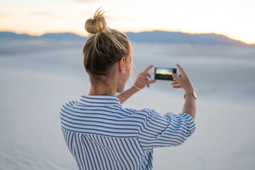 Wall Mural - back view of young woman using smartphone for making selfie standing at beautiful white sand dunes a