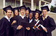© Studio Romantic - Group of happy diverse multiracial multiethnic college or university buddies wearing black student caps and gowns, with diplomas in hands, celebrating their graduation day and having fun together