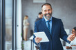 © Dragana Gordic - Portrait of a mature businessman using a digital tablet in a modern office with his colleagues in the background. Cropped shot of a mature businessman working on his tablet in the office