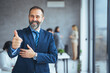 © Dragana Gordic - Cheerful businessman thumbs up posing and smiling at camera.  Portrait of happy business man looking at camera with copy space. Satisfied proud man feeling confident in a modern office.