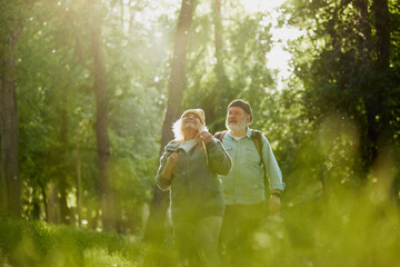 Senior couple, man and woman taking peaceful walk in park, enjoying tranquility and the beauty of nature. Sunlight and greenery. Concept of sport, aging, active and healthy lifestyle, health care