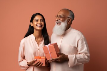 Wall Mural - Portrait of a blissful indian man and his daugther holding a gift while standing against minimalist or empty room background