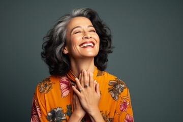 Wall Mural - Portrait of a joyful woman in her 50s joining palms in a gesture of gratitude isolated on solid color backdrop