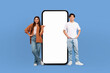 © Prostock-studio - With joyful faces, the young multiracial man and woman pose beside a blank-screened, life-sized smartphone, emphasizing the endless possibilities for customization.