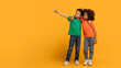 © Prostock-studio - Two African American children are standing on a bright yellow background, both pointing in the same direction, panorama with copy space