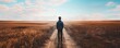 © Rattanathip - A person stands alone on a dirt path in the middle of a vast golden field, under a blue sky with scattered clouds, embracing solitude.