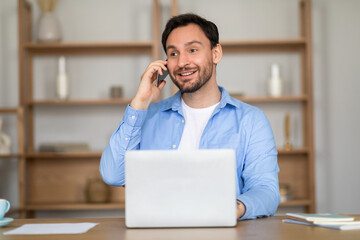 Poster - A man sitting at a desk, engaged in a phone conversation. He is multitasking, with a laptop open in front of him.