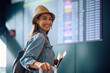 © Drazen - Young happy woman checking her flight schedule at airport and looking at camera.