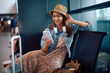 Wall Mural - Happy woman using smart phone while waiting for her flight at departure area.