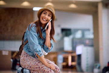 Wall Mural - Happy female traveler talking on phone at departure area.