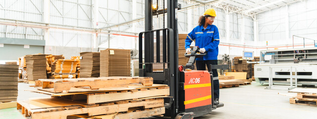 African American female worker driving forklift truck in heavy metal industrial factory, Smiling woman engineer wearing vest and helmet safety moving material at warehouse factory