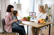 © sofiko14 - Mother with little girl at appointment with family nutritionist. Mature experienced female doctor showing tablet with gastrointestinal tract image for treatment planning to little female child.
