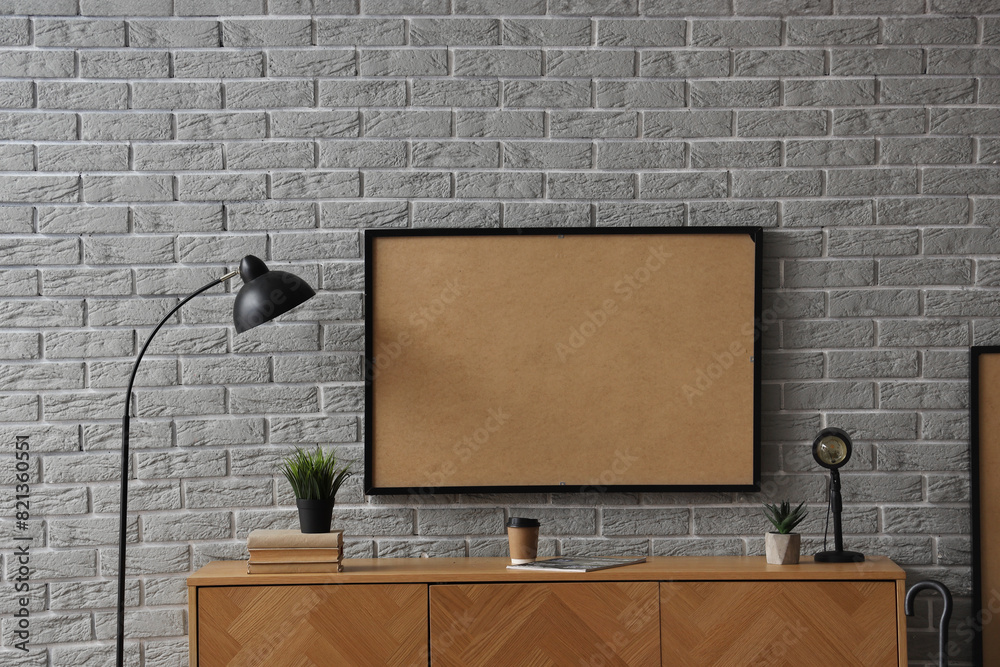 Wooden cabinet with frame and lamp near grey brick wall