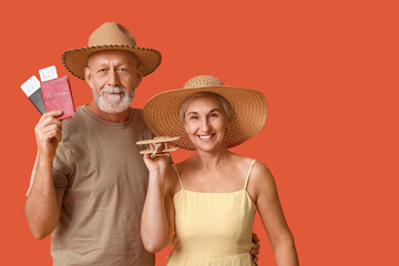 Mature couple of travelers with passports and wooden airplane on orange background