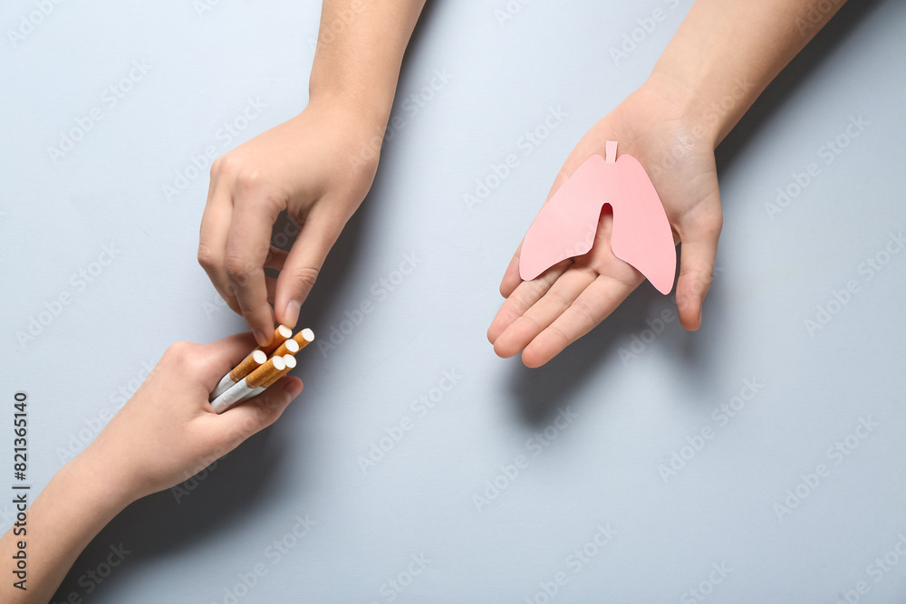 Female hands with paper lungs and cigarettes on grey background