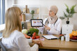 © sofiko14 - Muslim female doctor showing on tablet graphs of food for healthy eating. Mature lady patient visiting arabian woman nutritionist in hijab at modern clinic.