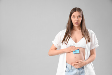 Canvas Print - Shocked young pregnant woman and paper with word BOY on her belly against light background