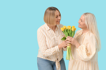 Wall Mural - Adult woman greeting her mother with bouquet of tulips on blue background. International Women's Day celebration