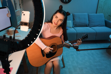 Wall Mural - Female student with guitar and microphone streaming at home in evening