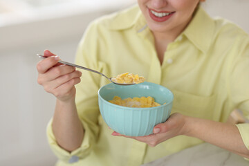 Sticker - Smiling woman eating tasty cornflakes at breakfast on blurred background, closeup