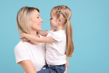 Wall Mural - Family portrait of happy mother and daughter on light blue background. Space for text