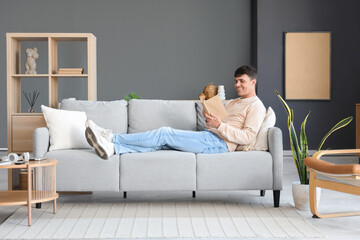 Wall Mural - Young man reading book on sofa at home