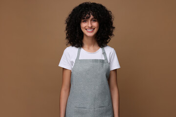 Wall Mural - Happy woman wearing kitchen apron on brown background. Mockup for design