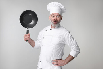 Wall Mural - Surprised chef in uniform holding wok on grey background