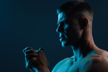 Poster - Muscular model sports young man on dark background. Fashion portrait of strong brutal guy. Male flexing his muscles.