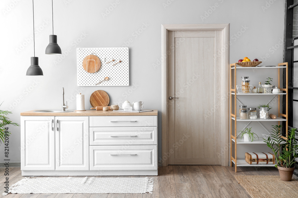 Interior of beautiful kitchen with white counters, door, shelving unit and lamp