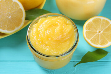 Wall Mural - Delicious lemon curd in glass jar, fresh citrus fruit and green leaves on light blue wooden table, closeup